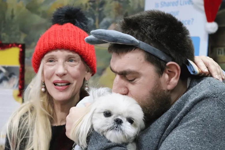 care worker photographed, smiling at the camera with someone they support who is cuddling a dog at a community event