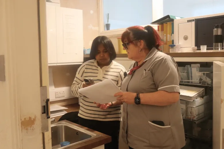 young care worker looking at a medication sheet with a senior member of staff and taking notes on their phone