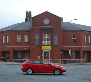 long shot of the bury adult learning centre, a red car is pictures driving past in front of the building