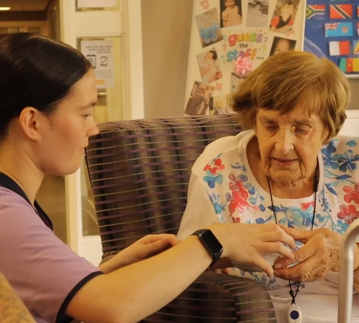 Support worker assisting an older adult with a cup of tea in a care home setting.