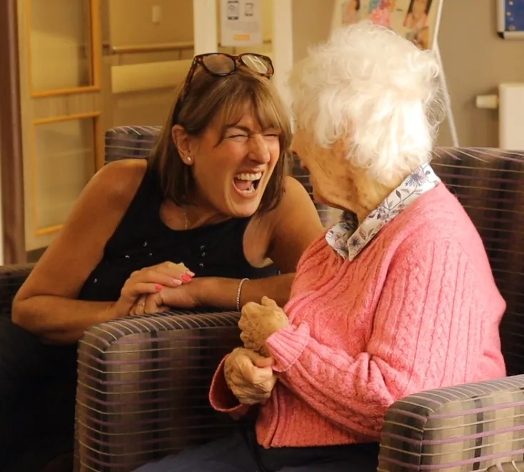 Support worker communicating with an older adult while providing support in a residential care setting.