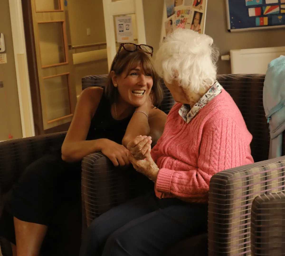 care worker sat smiling and talking to elderly resident in a care home