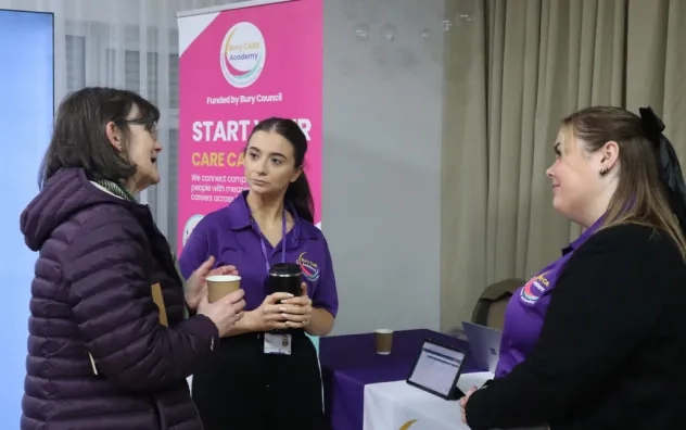Two members of the Bury Care Academy team stood speaking to a care provider