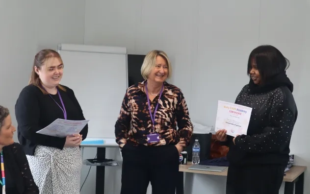 Two members of the Bury Care Academy team pictured smiling as they give a certificate over to one of the participants on the course