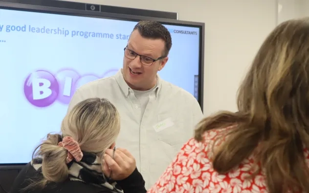 Two LEAD Programme attendees engaged in a conversation, Power Point board in the background reads 