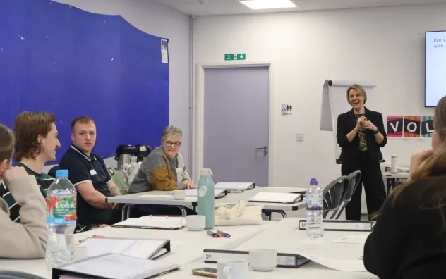 Long shot of LEAD Trainer smiling and speaking to a participant while the rest of the participants look on