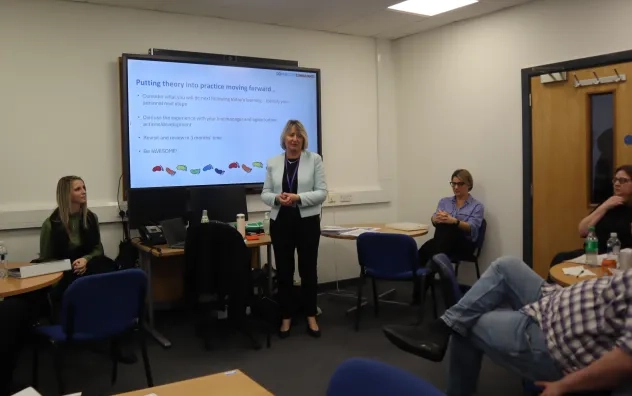 Bury Care Academy manager speaking to the learners and the end of the programme. She is stood in the middle of the room with the learners and lead trainer looking towards her.