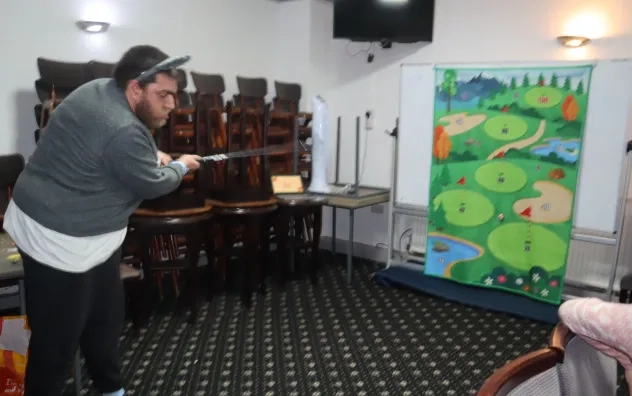 A man at the persona Christmas Fair playing a golf driving range game, he is shown hitting the golf ball and aiming for a poster that displays all the different targets